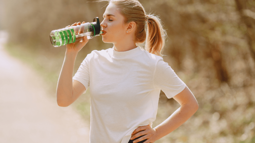 A person is drinking water from a bottle in the woods
