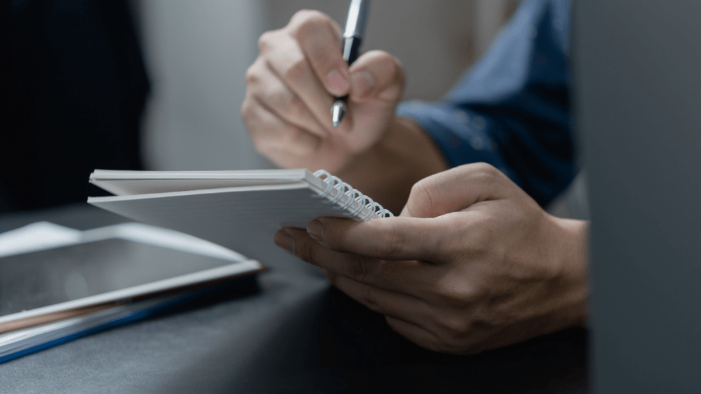 a person is writing in a notebook while sitting at a desk