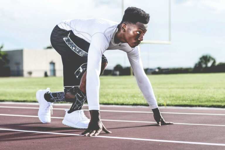 Focused athlete in starting position on a sunny track field, ready to sprint.